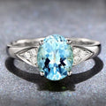Close-up of a woman's court style ring with a detailed heart pattern inlaid in a blue natural zircon stone.