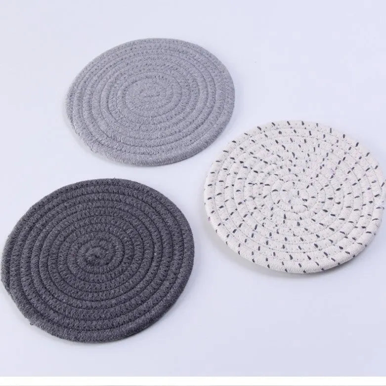 Three round grey cotton cord coasters on a wooden table