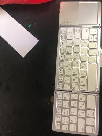 Black tri-fold folding Bluetooth keyboard with touchpad, shown both folded and unfolded next to a mobile phone.