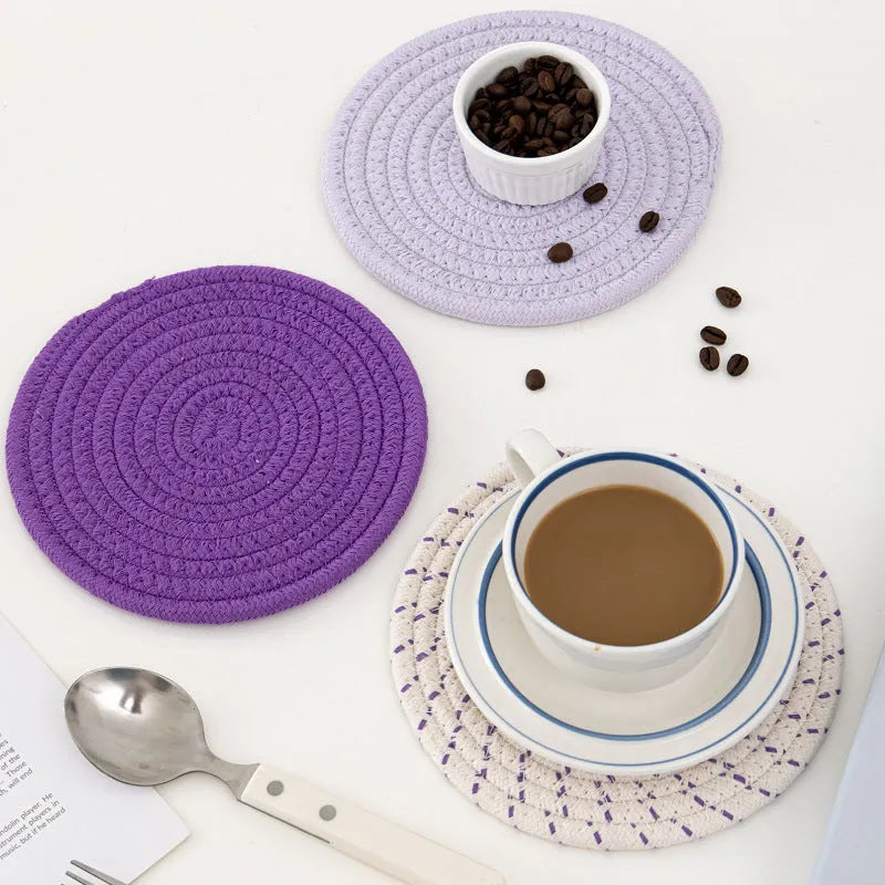 Three round grey cotton cord coasters on a wooden table