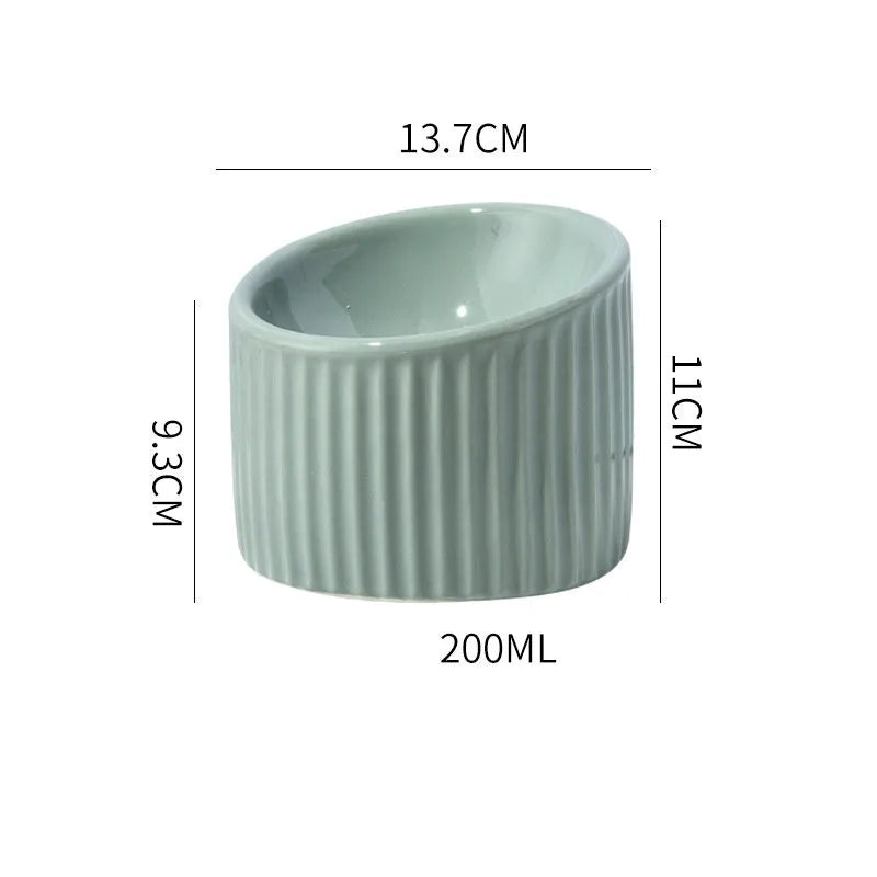 Ceramic elevated cat bowl in light green, showing its tilted, round shape and raised design on a table.