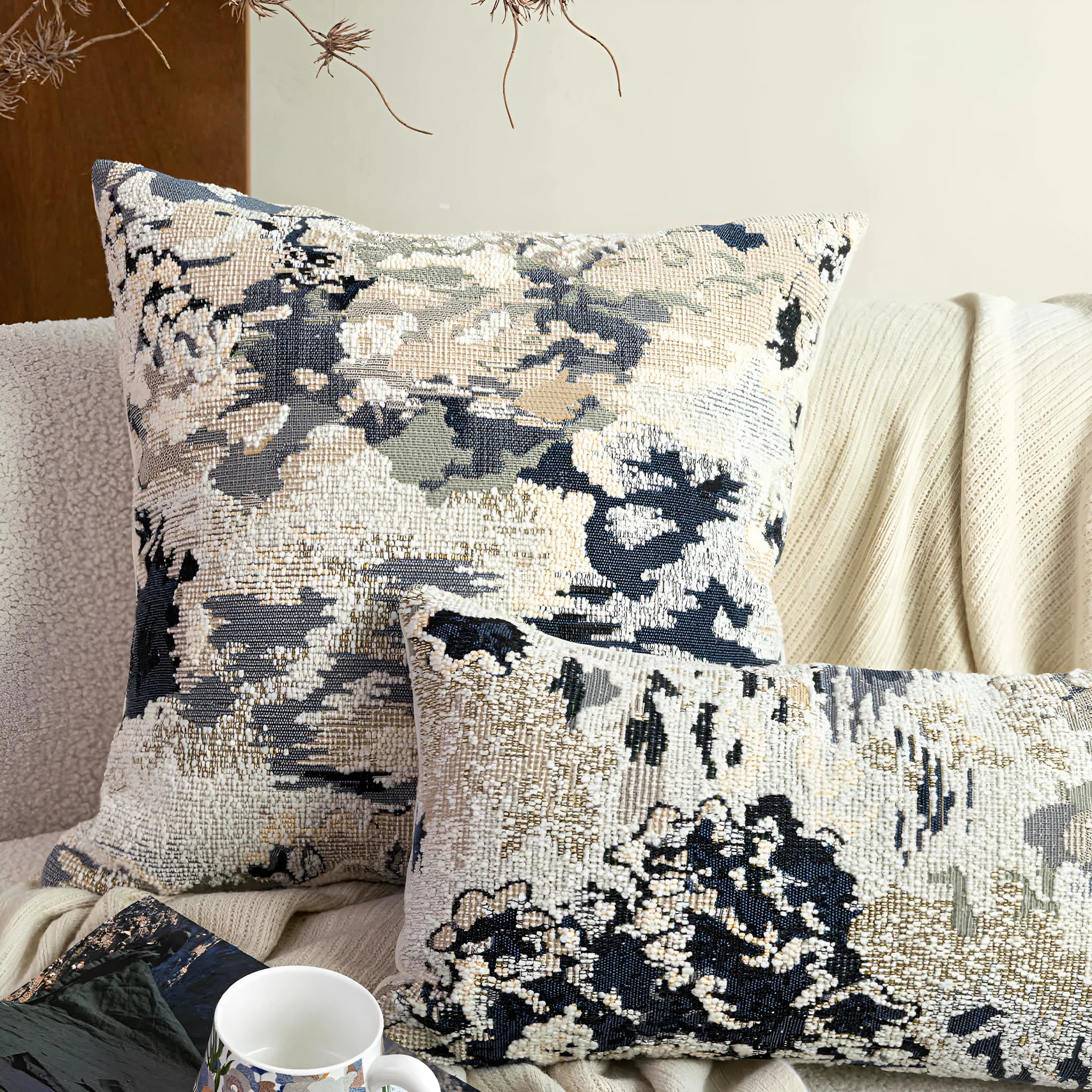Antique blue square cushion with abstract botanical flower pattern on a grey sofa.