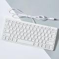 Compact wired USB keyboard in black, white, pink, or blue on a desk next to a laptop.