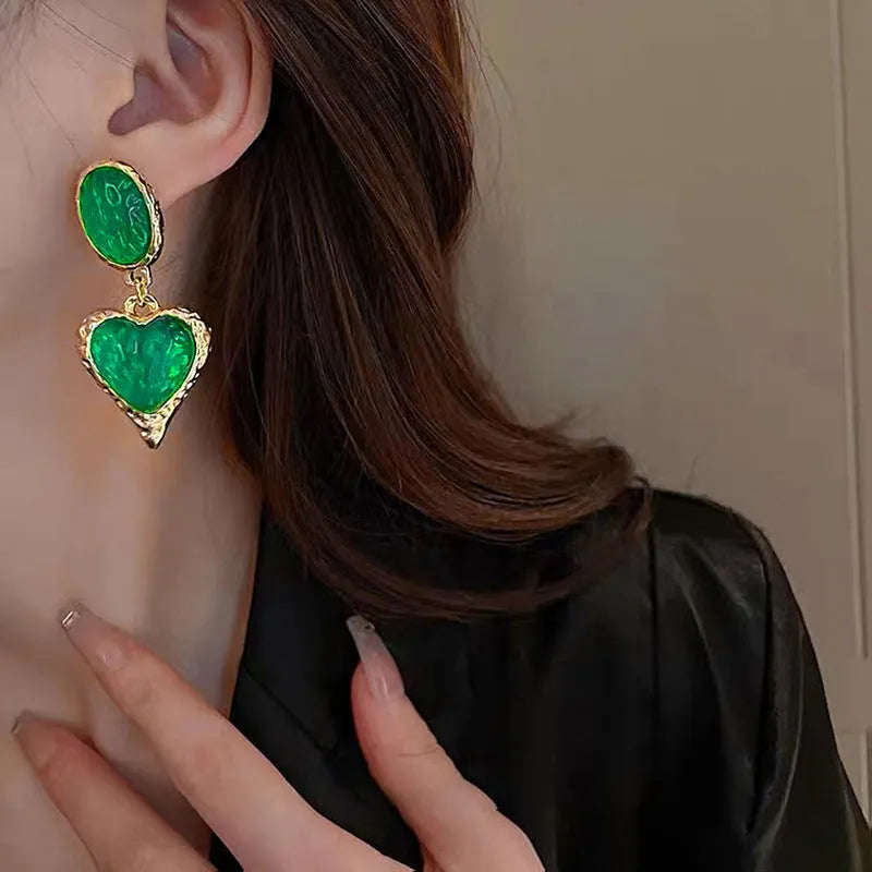 Close-up of oval love heart stud earrings with pleated needle posts in green, purple, red, and yellow-white colours.