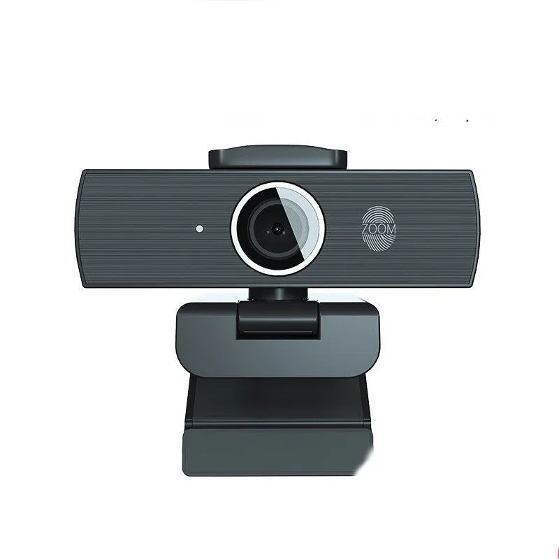 Black USB webcam with magnetic privacy cover on a desk next to a laptop.