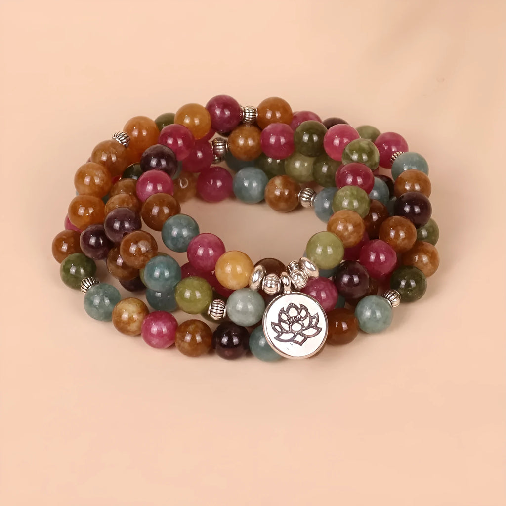 Close-up of a multi-layer beaded bracelet with 108 alloy beads and a central lotus pendant in a tourmaline colour.