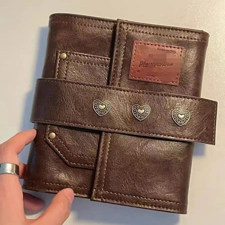 Brown A7 size notebook with a retro leather-look PU cover and metal buckle closure, lying open on a desk.