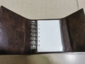 Brown A7 size notebook with a retro leather-look PU cover and metal buckle closure, lying open on a desk.