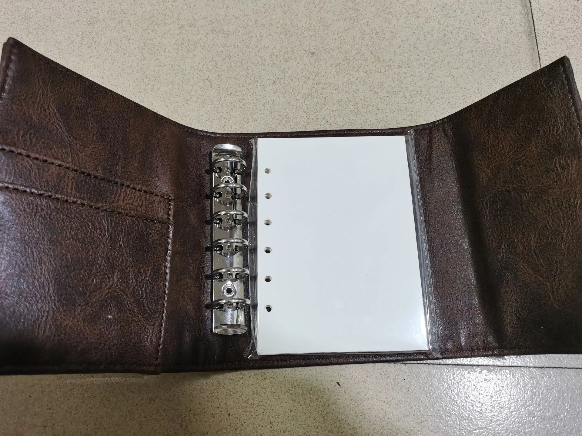 Brown A7 size notebook with a retro leather-look PU cover and metal buckle closure, lying open on a desk.