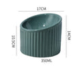 Ceramic elevated cat bowl in light green, showing its tilted, round shape and raised design on a table.