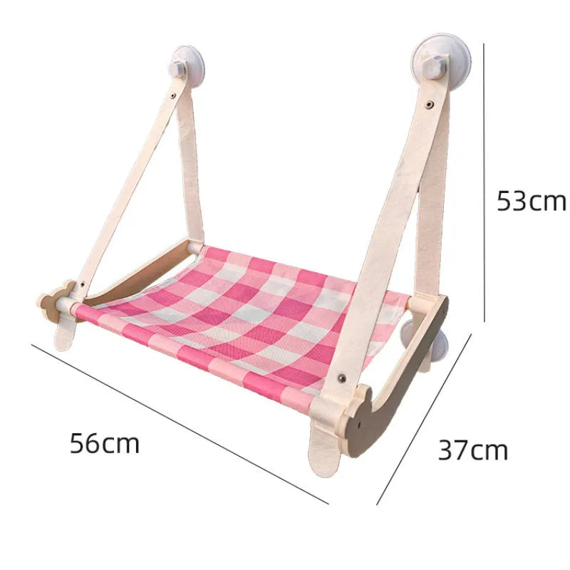 Pink wooden cat hammock with suction cups attached to a window, showing a removable cat paw print fabric seat.
