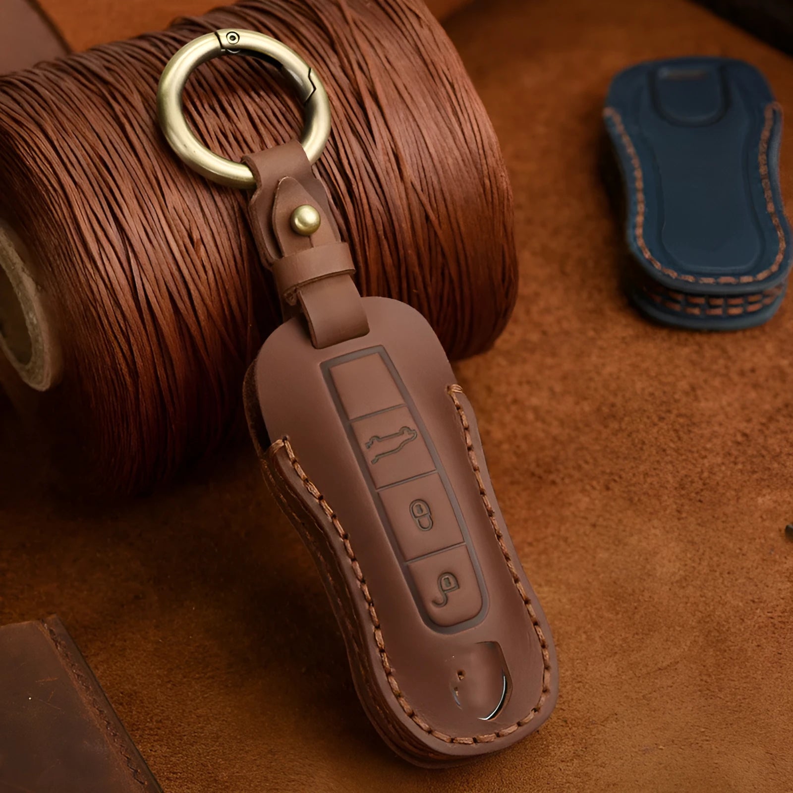 Brown cowhide leather Porsche key cover with a retro metal buckle, shown alongside keys.