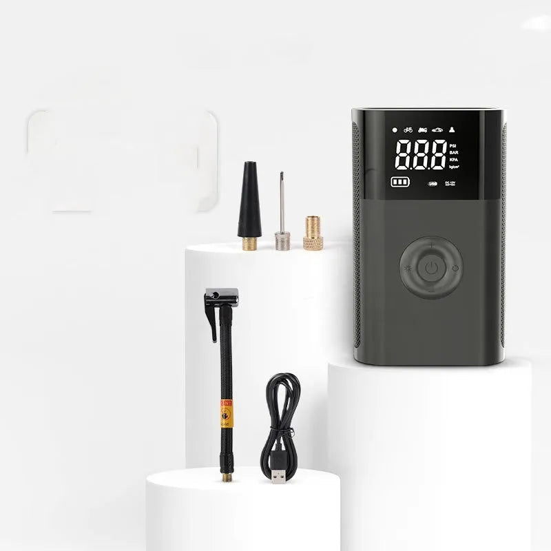 Handheld wireless digital tyre inflator with display screen, LED light, and multiple nozzle adaptors on a table.