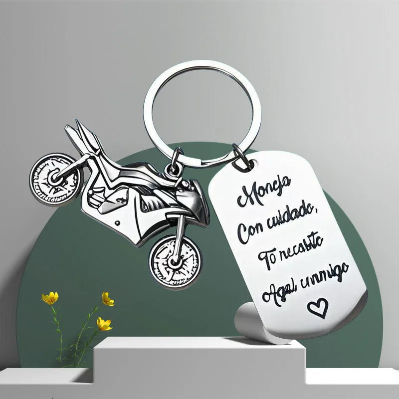 Silver motorcycle charm on a stainless steel key ring next to a red flannel storage bag.