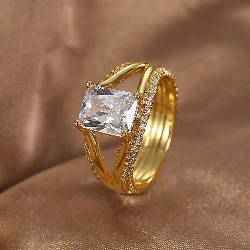 Gold-colour geometric women's ring with a square zircon centre, shown on a finger.