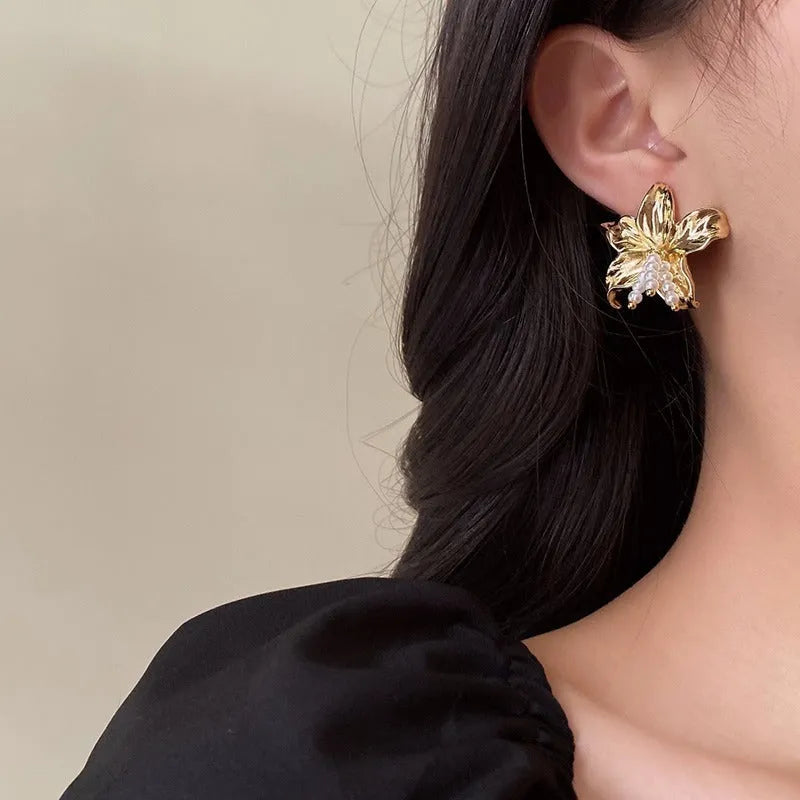 A pair of exaggerated gold metal flower earrings with pearl details, showing a niche jewellery style.