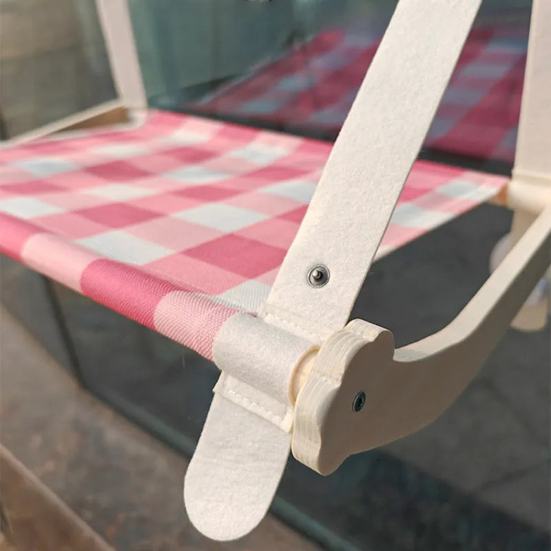 Pink wooden cat hammock with suction cups attached to a window, showing a removable cat paw print fabric seat.