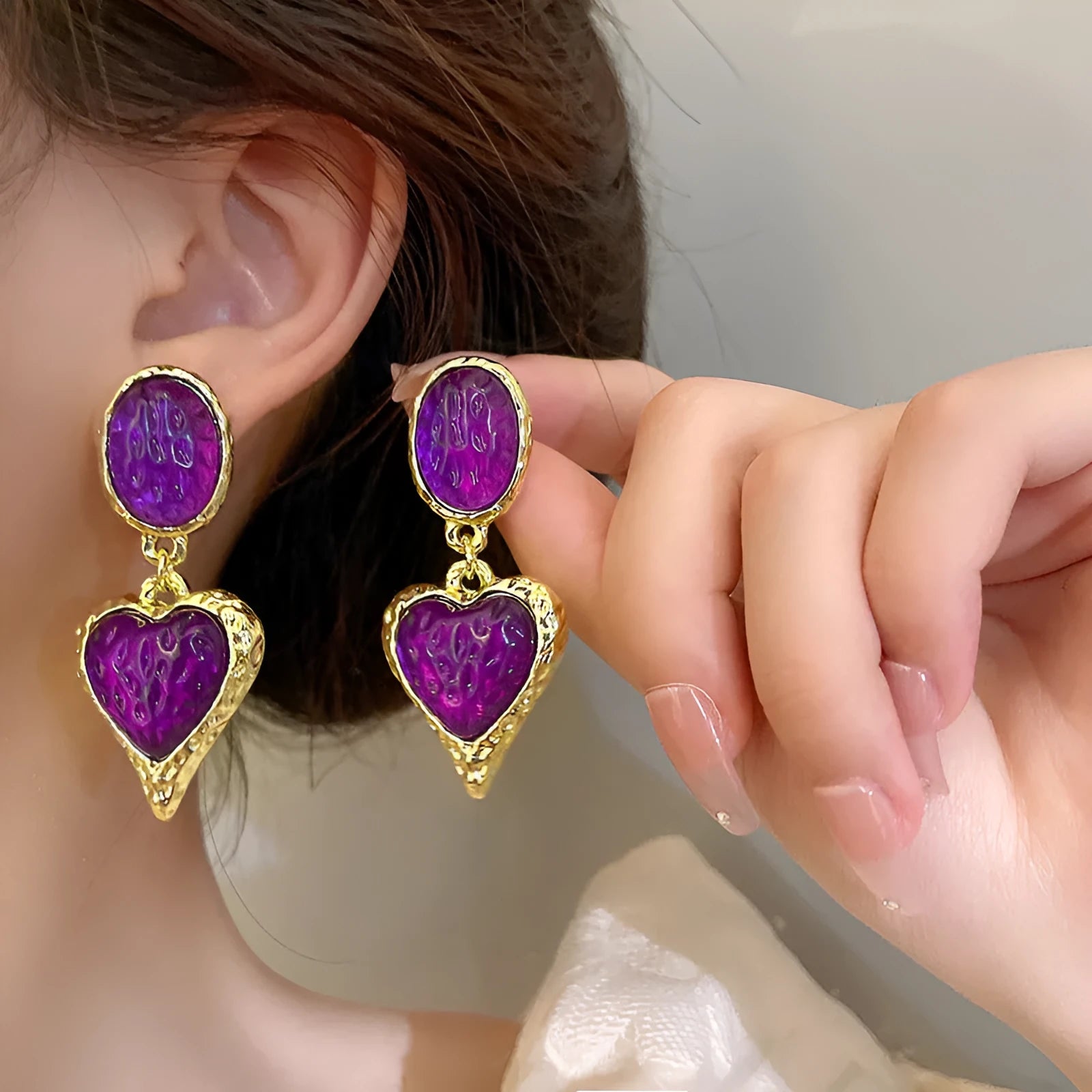 Close-up of oval love heart stud earrings with pleated needle posts in green, purple, red, and yellow-white colours.