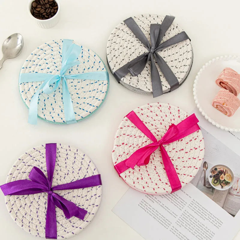Three round grey cotton cord coasters on a wooden table