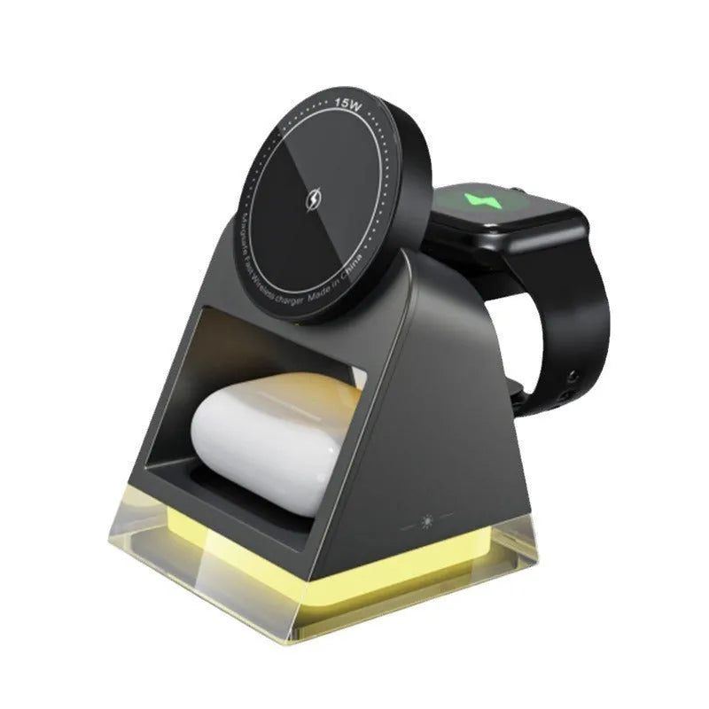 Black three-in-one magnetic wireless charger with night lamp charging phone, watch, and headset on a desk